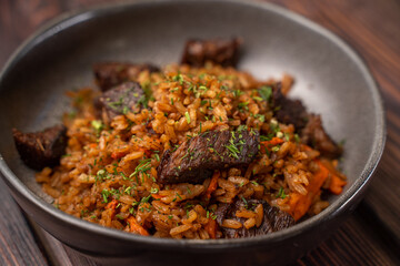 Traditional pilaf with meat in a black plate on a wooden background