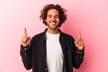 Young caucasian man isolated on pink bakcground indicates with both fore fingers up showing a blank...