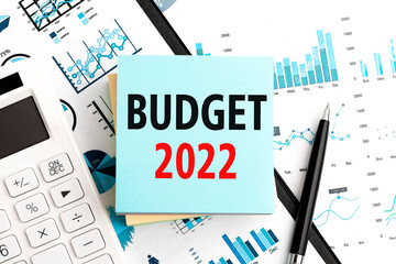 Text BUDGET 2022 on stickers. Pen and calculator on clipboard with charts, documents and graphs....