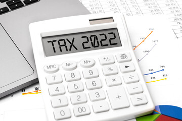 Text TAX 2022. Calculating machine, laptop and charts, documents and graphs top view. Business and tax concept on white background.