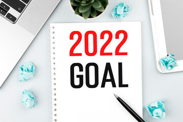 Text 2022 GOAL on card. Laptop, pieces of paper, pen and plant on office desk. Flat lay, top view. Planning concept.