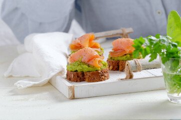 Sandwich of salmon avocado cream on white wooden background.
