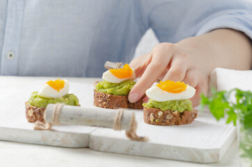 Female hand holds sandwich of avocado cream with egg on light background.