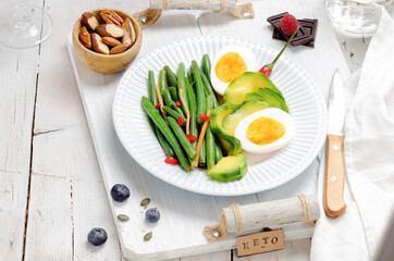 Fototapeta na wymiar Green beans with avocado, egg and spices in a white dish on light background. Keto diet.