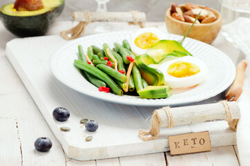 Green beans with avocado, egg and spices in a white dish on light background. Keto diet.
