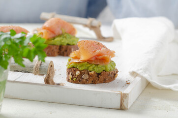 Bruschetta with cream of avocado and salmon on white wooden background.