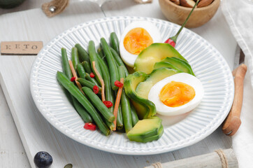 Green beans with avocado, egg and spices in a white dish on light background. Keto diet.