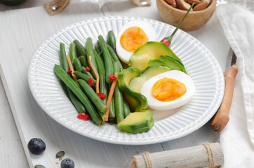 Green beans with avocado, egg and spices in a white dish on light background. Keto diet.