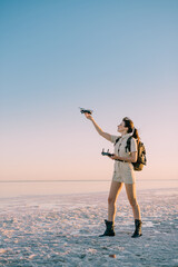 Fototapeta premium Quadcopter launch. Young woman tourist holds a drone in his hand lifting it up. Full-length side view.