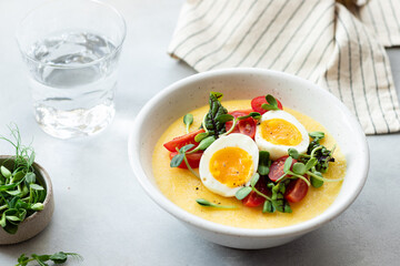 creamy polenta with eggs, fresh vegetables, microgreens on gray table. Italian cuisine concept. close-up