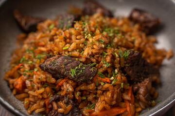 Traditional pilaf with meat in a black plate on a wooden background