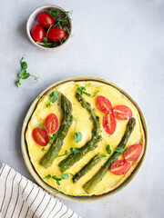 healthy omelette with asparagus, tomatoes and green pea microgreens on a gray background with copy space. Italian cuisine concept. vertical image