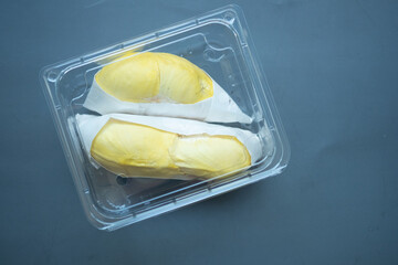 Golden yellow durian in a clear plastic box with a black background.