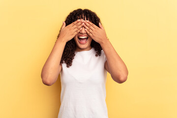 Young mixed race woman isolated on yellow background covers eyes with hands, smiles broadly waiting for a surprise.