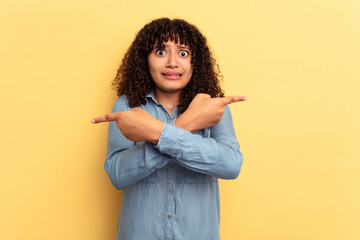 Young mixed race woman isolated on yellow background points sideways, is trying to choose between two options.