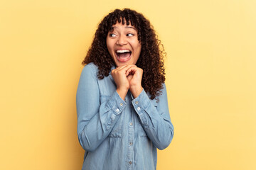 Young mixed race woman isolated on yellow background keeps hands under chin, is looking happily aside.