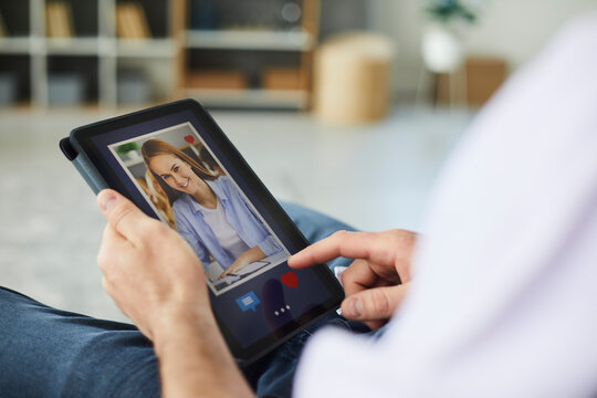Closeup man looking at photo of attractive woman on tablet display. Young guy presses red like button and sends message to girl on online dating website or mobile app. Hands holding tablet in close up