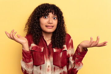 Young mixed race woman isolated on yellow background doubting and shrugging shoulders in...