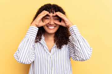 Young mixed race woman isolated on yellow background showing okay sign over eyes