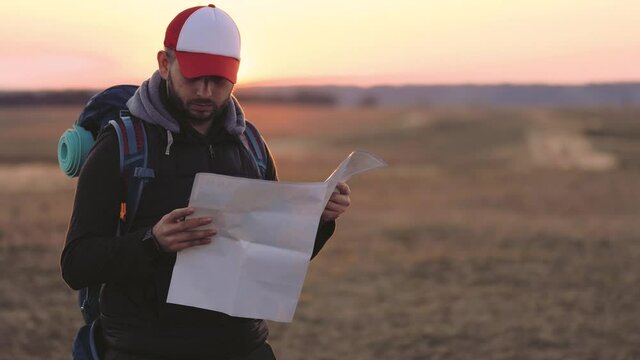 Adventure man with map and extreme explorer gear on mountain with sunset. Young man with backpack and map enjoying sunset, looking map. Tourist traveler on background landscape and sunlight in trip
