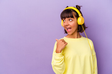 Young mixed race woman listening to music isolated on purple background points with thumb finger away, laughing and carefree.