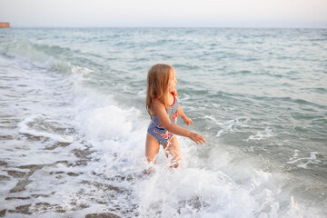 little girl in a striped swimsuit playing on the waves in the sea
