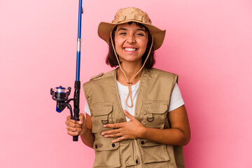 Young mixed race fisherwoman holding a rod isolated on pink background laughing and having fun.