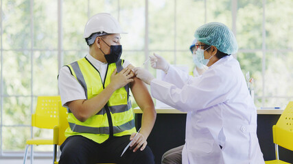 COVID-19 Vaccination station in construction industry. Doctor are vaccinating to group engineer...