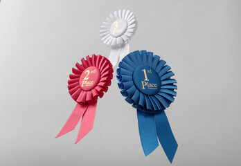 Three rosettes fly over gray background as prizes to winners and champions for quality and victory.
