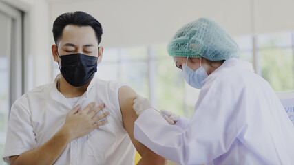 COVID-19 Vaccination station. Doctor or nurse are vaccinating man patient protect COVID-19 or flu in hospital room. People wear face mask protection from virus disease at clinic or hospital office