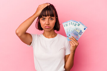 Young mixed race woman holding bills isolated on pink background being shocked, she has remembered important meeting.