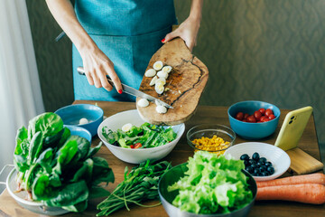 An unrecognizable woman chef prepares a salad and puts the ingredients in a large bowl. The concept of healthy eating and cooking at home.