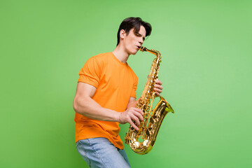 Photo of joyful happy young man artist play saxophone good mood wear jeans isolated on green color background - obrazy, fototapety, plakaty