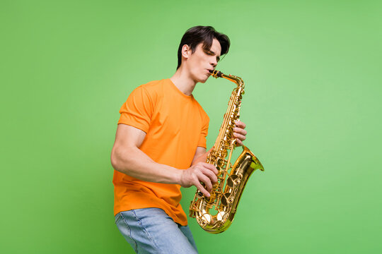 Photo of joyful happy young man artist play saxophone good mood wear jeans isolated on green color background