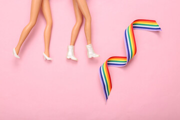 Lgbt community, lesbian relationship concept. Dolls feet and rainbow lgbt symbol ribbon on pink background