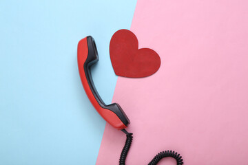 Retro telephone receiver with red heart on blue-pink pastel background. Top view