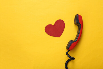 Retro phone receiver with red heart on yellow background. Top view