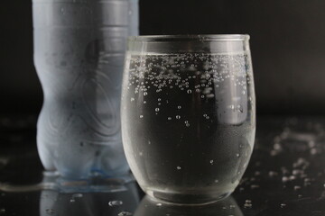 The mineral cold water in the glass and in the plastic bottle stand next to the black background with a place to insert and with a copypispe. drinking water