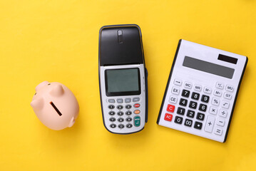 Pos terminal, calculator and piggy bank on a yellow background. Top view