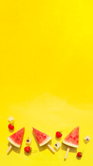 screen saver, background for stories, banner of watermelon slices on sticks, ice cubes and strawberries on a bright yellow background. copy space.