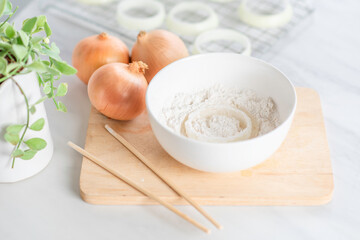 Fresh raw onion rings and flour on cutting board. 