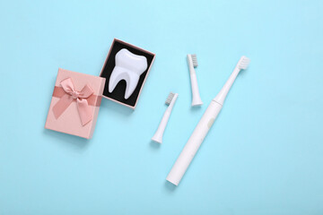 Ultrasonic plastic toothbrush with replaceable heads and tooth model in gift box on blue background. Dental care concept. Top view