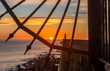Tynemouth Pier and the Lighthouse through the metal railings with a beautiful vibrant sunrise