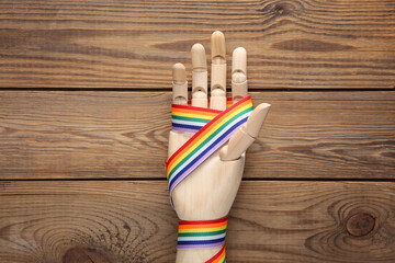 Wooden hand with LGBT rainbow ribbon pride tape symbol on wooden background. Top view