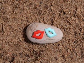 Red and blue polypastry lips lie on a rock in the sand.              