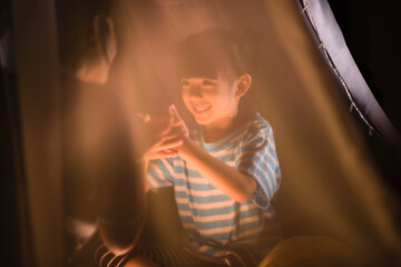 a little girl playing hand shadow art with her mom in bedroom before sleeping time, family concept, cute kid smiling, asian family concept, playing in kid tent.