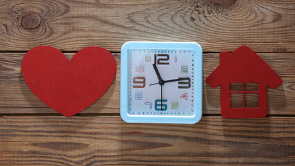 Alarm clock with red heart and house on wooden background. Top view