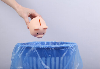 Hand throws piggy bank into trash bin with package on gray background