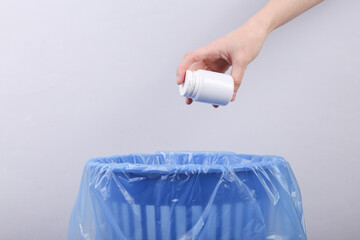 Hand throws pills bottle into trash bin with package on gray background