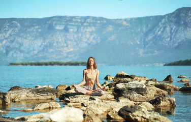 Fototapeta na wymiar Woman yoga in nature with beautiful mountains landscape, girl sitting on stones in Lotus pose